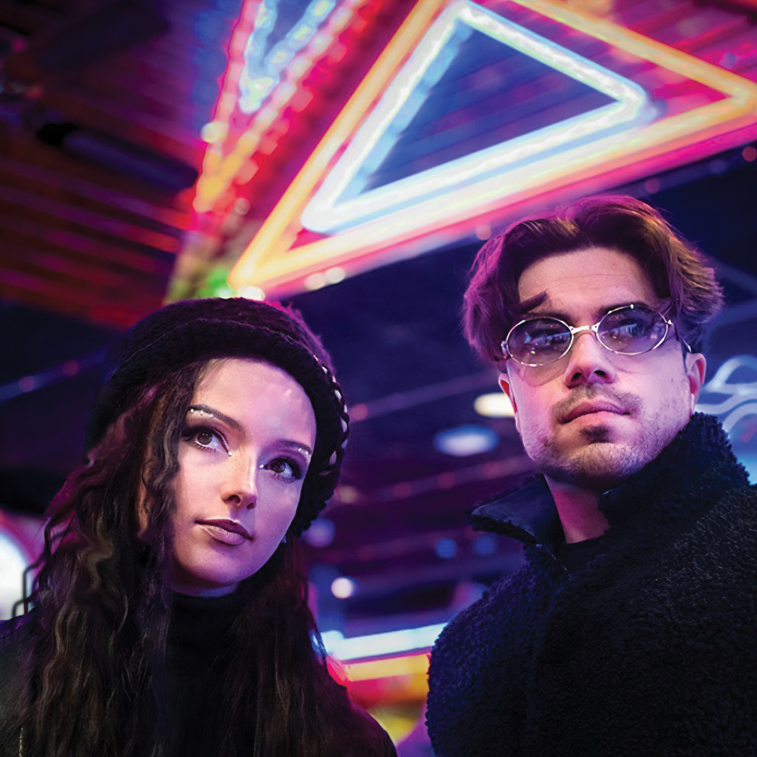 The two band members standing in front of colourful lights
